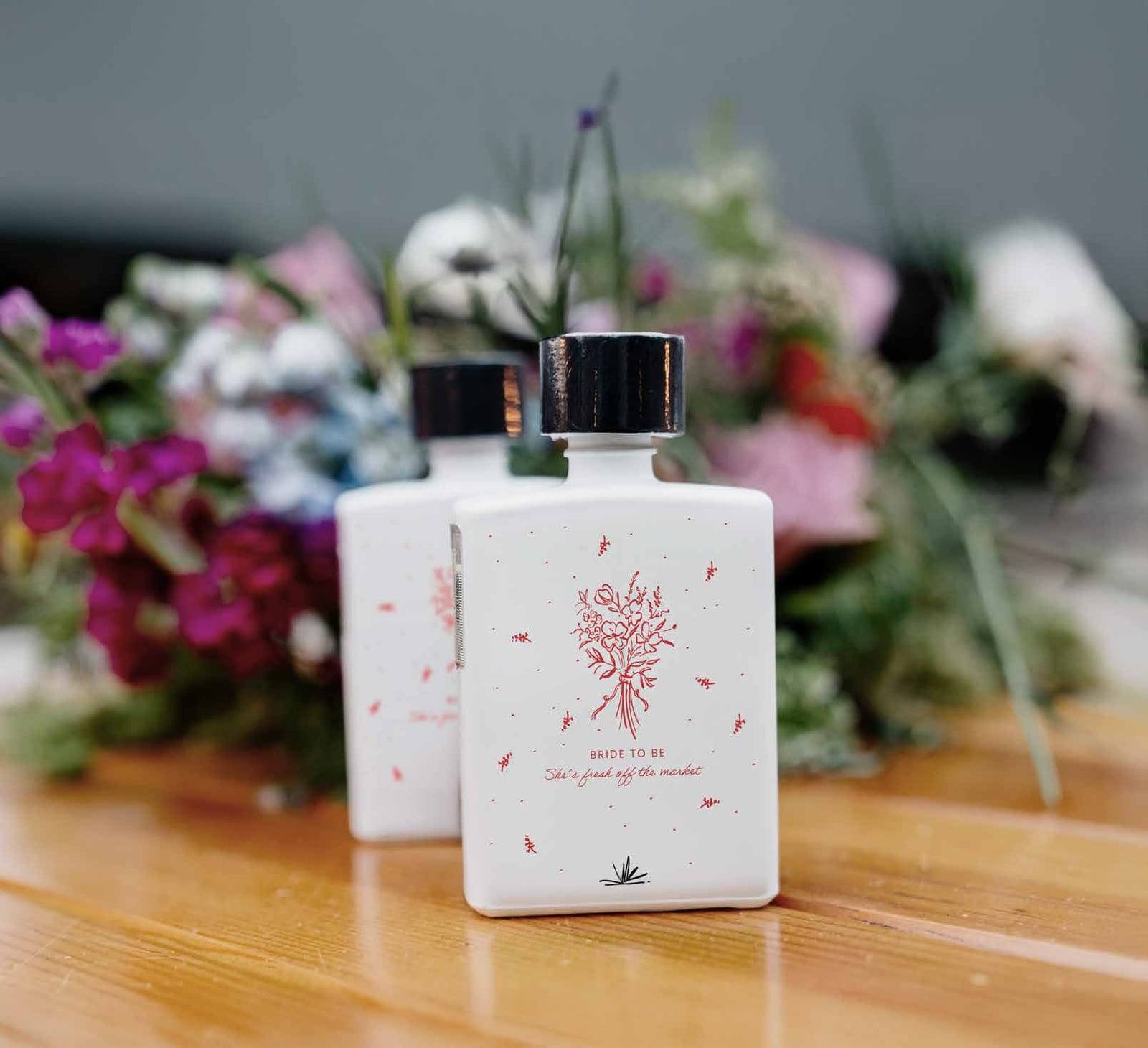 Botella blanca con ilustración floral sobre una mesa con flores